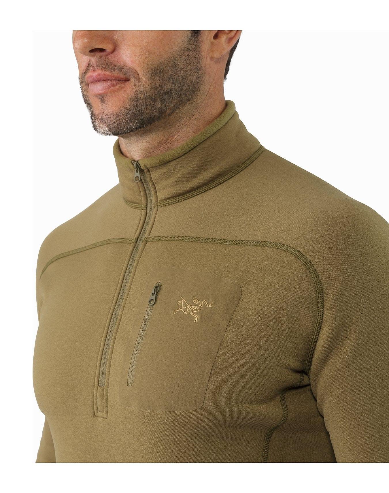 Ein Mann trägt einen olivgrünen ARC'TERYX LEAF Cold WX Zip Neck SV - Crocodile Fleece mit einer Brusttasche und einem gestickten Logo auf der linken Brustseite, von den Schultern aufwärts, leicht nach links gewandt.