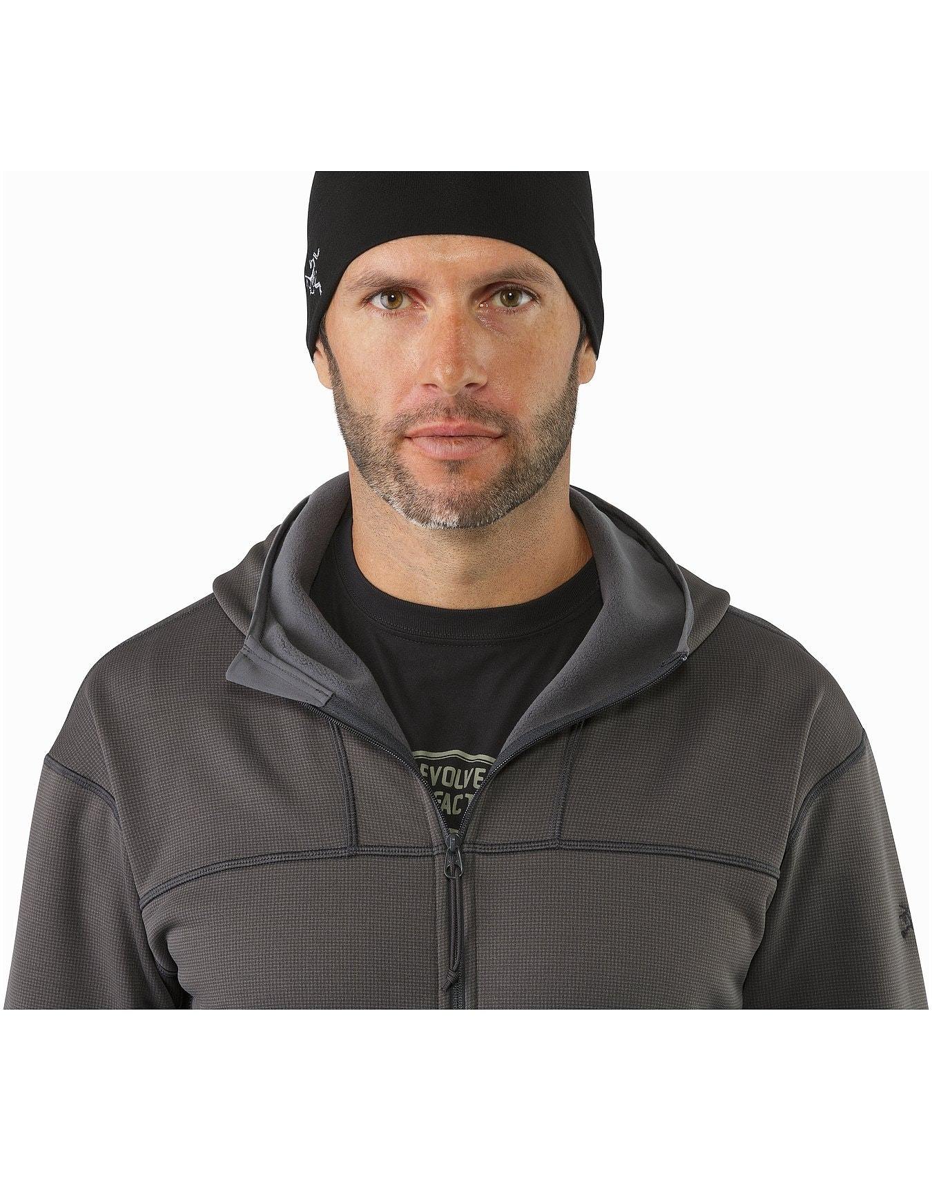 Ein Mann mit gestutztem Bart trägt eine schwarze Mütze und einen ARC'TERYX LEAF Naga Hoody Full Zip Gen2.1 - Wolf über einem schwarzen Hemd und steht vor einem schlichten weißen Hintergrund.