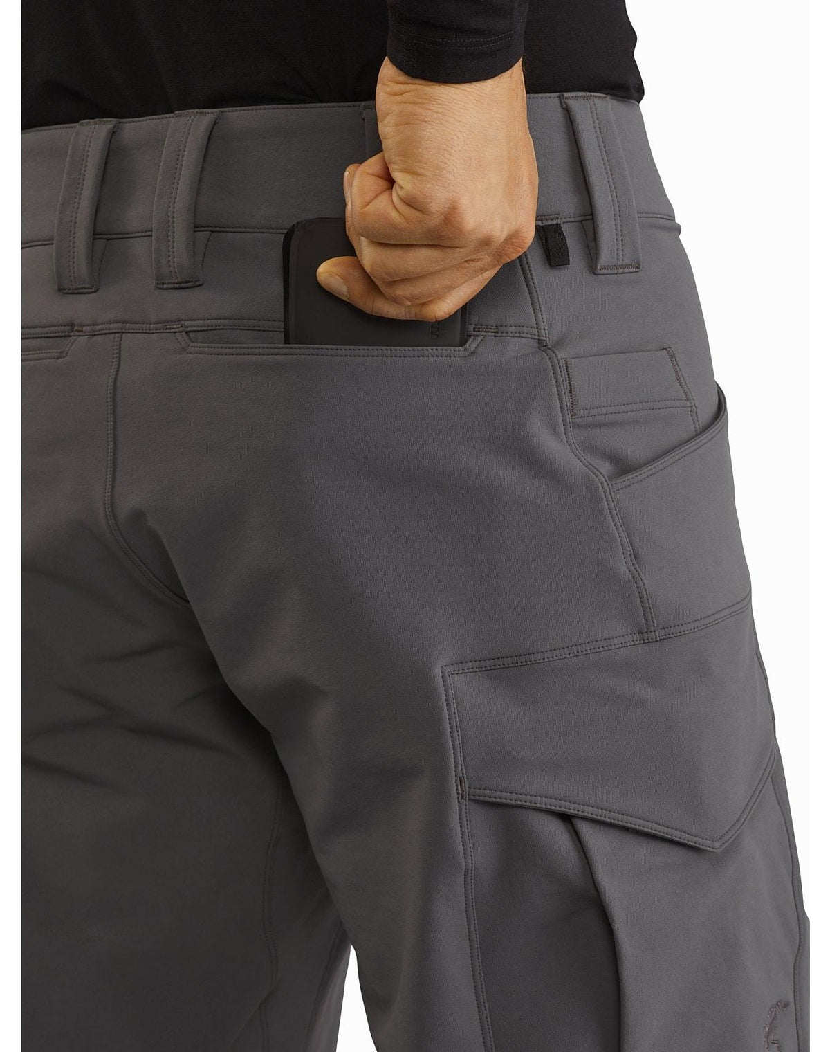 Eine Person in ARC'TERYX LEAF Arc'teryx Patrol Pant AR Men's - Wolf steckt mit der rechten Hand ein Smartphone in die Gesäßtasche. Das Bild hebt die Hose hervor und zeigt einen Teil eines schwarzen Hemdes.