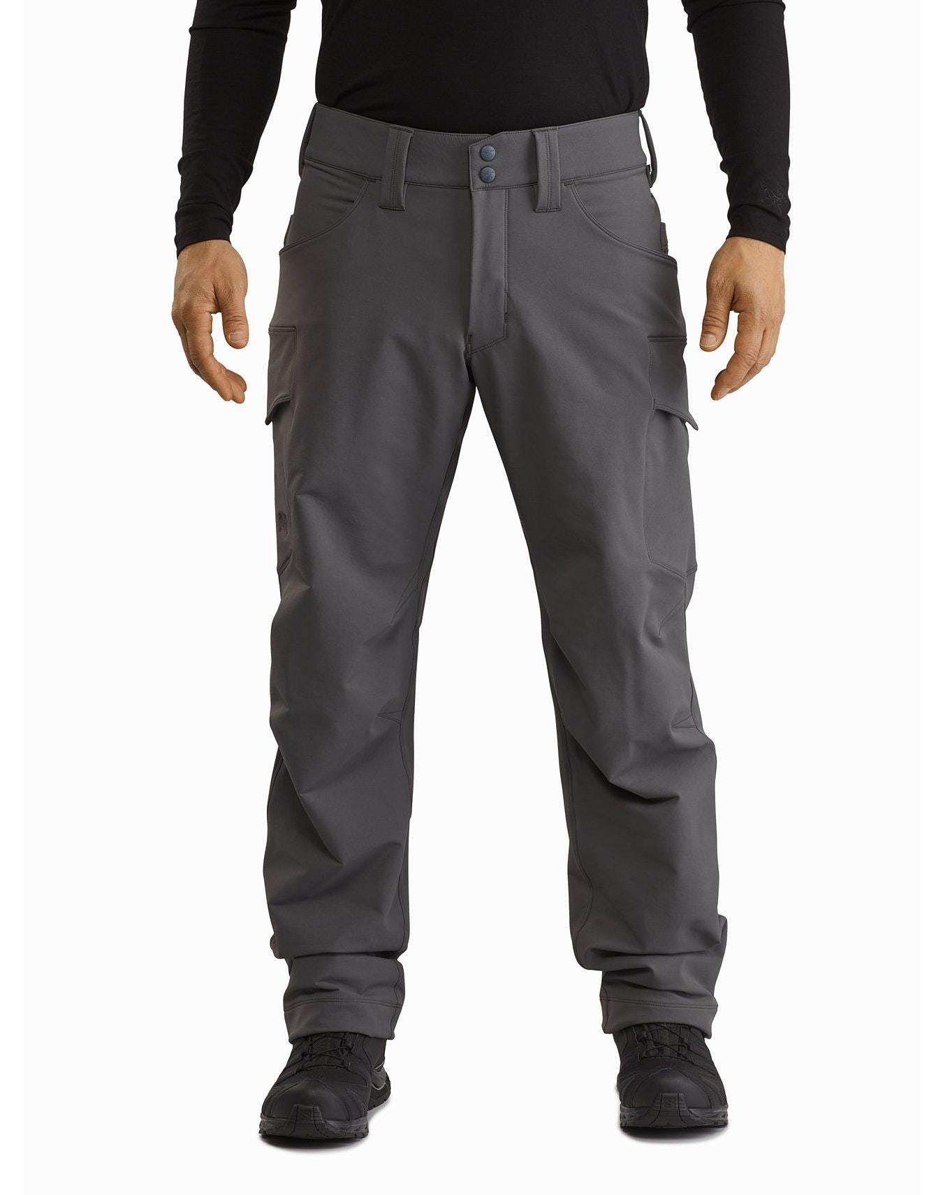 Eine Person trägt eine ARC'TERYX LEAF Arc'teryx Patrol Pant AR Men's - Wolf Cargohose mit mehreren Taschen, ein schwarzes langärmeliges Hemd und schwarze Schuhe, steht mit dem Gesicht nach vorne und den Armen leicht von der Seite entfernt.