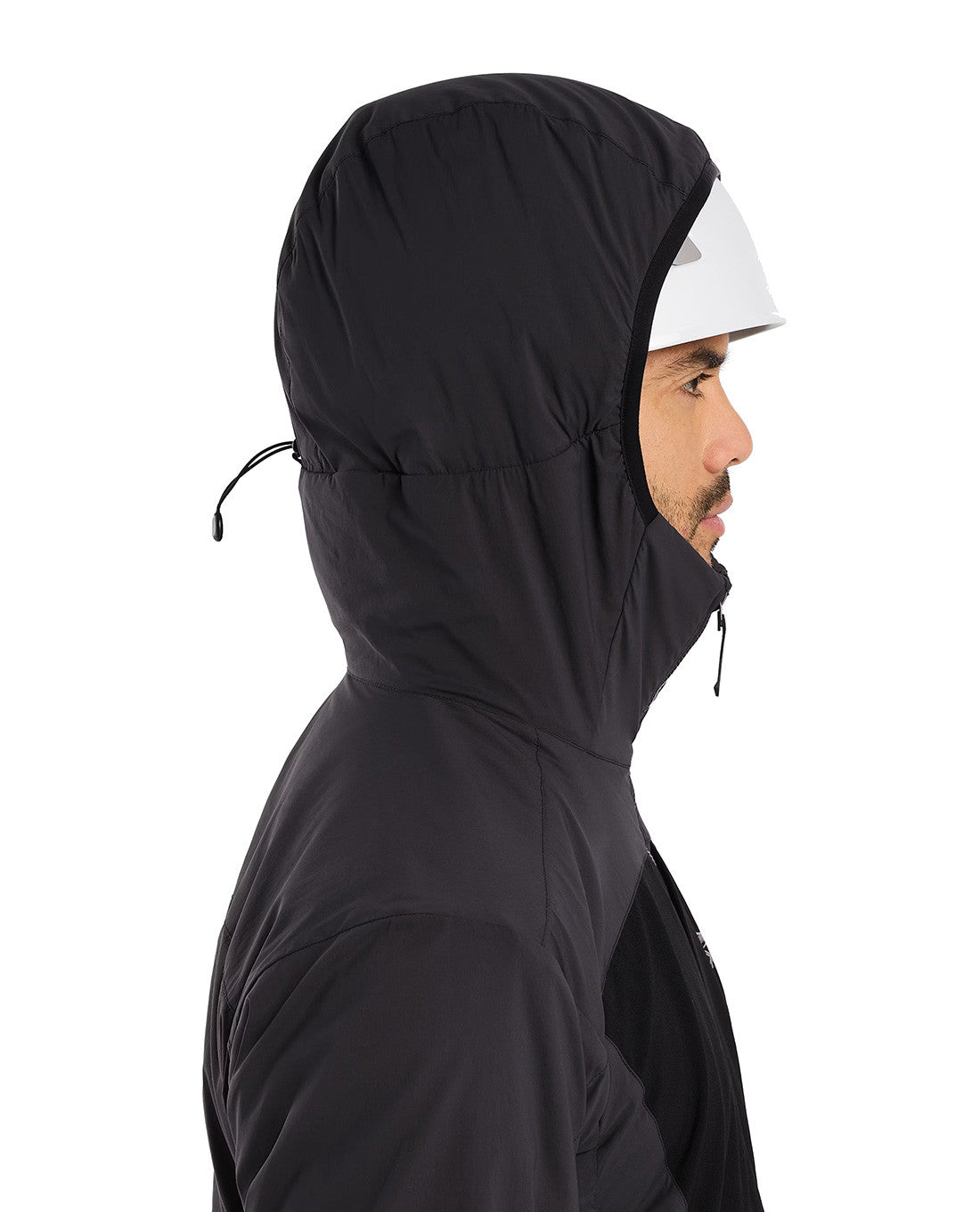 Ein Mann im Profil, der einen ARC'TERYX PRO Arc'teryx Practitioner AR Hoody Men's - Carbon Copy - einen schwarzen, atmungsaktiven Midlayer mit synthetischer Isolierung und einen weißen Helm trägt, steht vor einem schlichten weißen Hintergrund.
