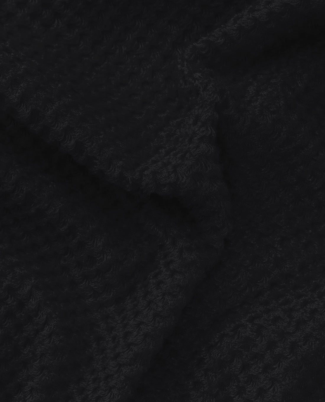 Eine Nahaufnahme des Arc'TERYX Practitioner AR Hoody Women's - Carbon Copy von ARC'TERYX PRO zeigt den strukturierten schwarzen Stoff, das weiche Webmuster und die subtilen Falten, die die Qualität und Tiefe dieses atmungsaktiven Midlayers hervorheben.