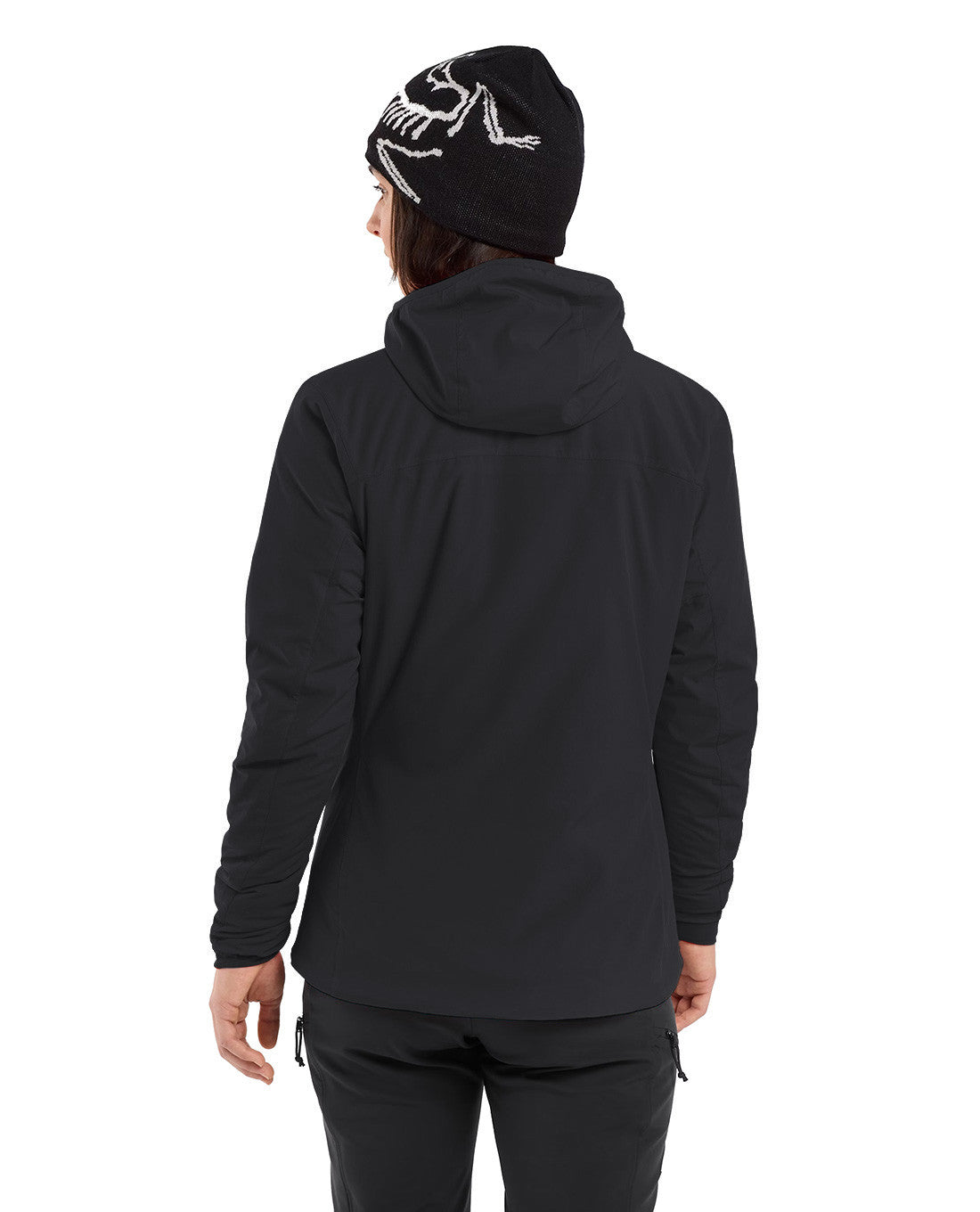 Rückenansicht einer Person in einem schwarzen ARC'TERYX PRO Practitioner AR Hoody Women's - Carbon Copy, einer schwarzen Hose und einer schwarzen Arc'teryx-Mütze mit weißem Logo vor einem weißen Hintergrund.
