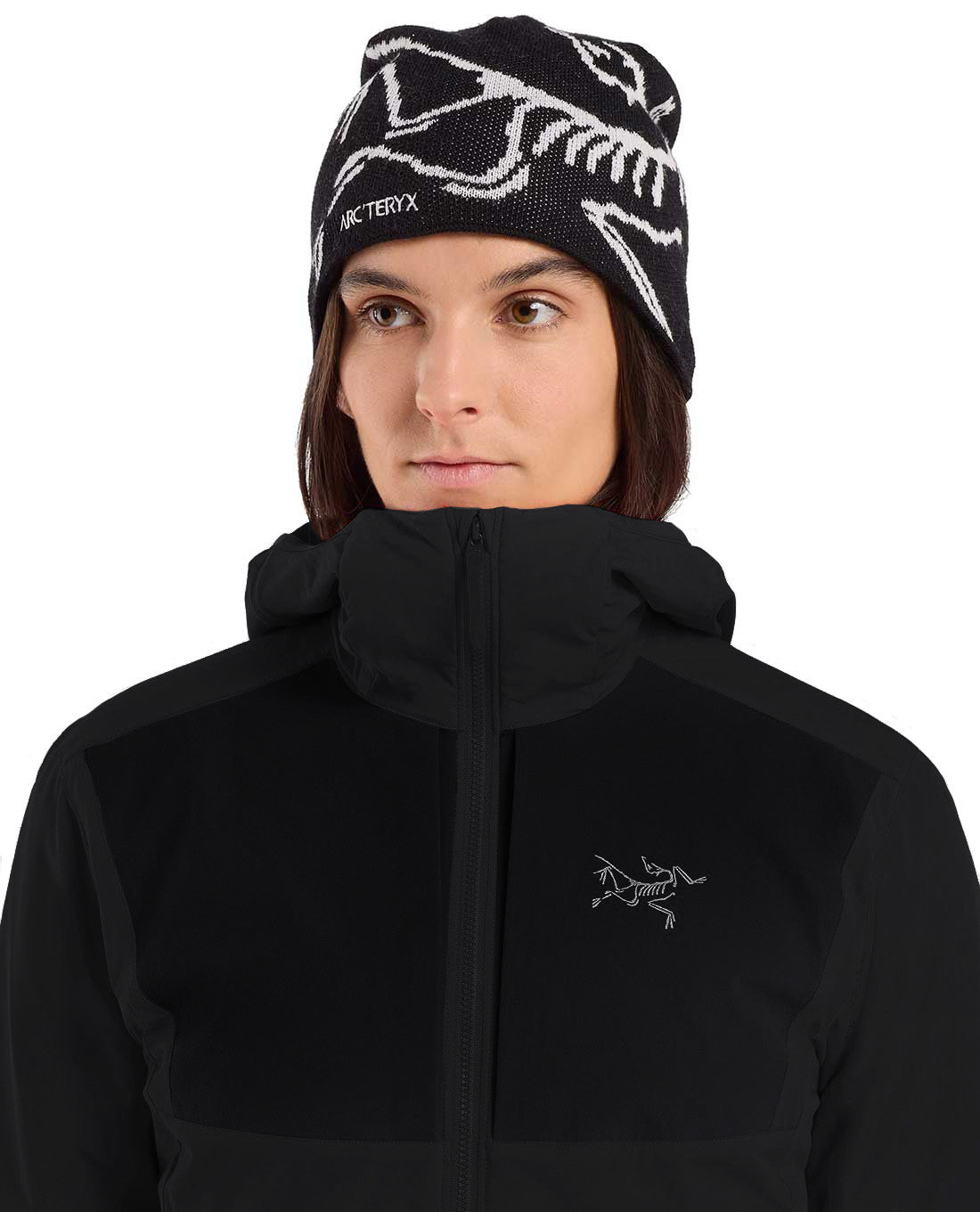 Das Model trägt einen ARC'TERYX PRO Practitioner AR Hoody Women's - Carbon Copy, einen luftigen Midlayer mit Logostickerei, gepaart mit einer schwarzen Strickmütze mit weißem Arcteryx-Grafikmuster.