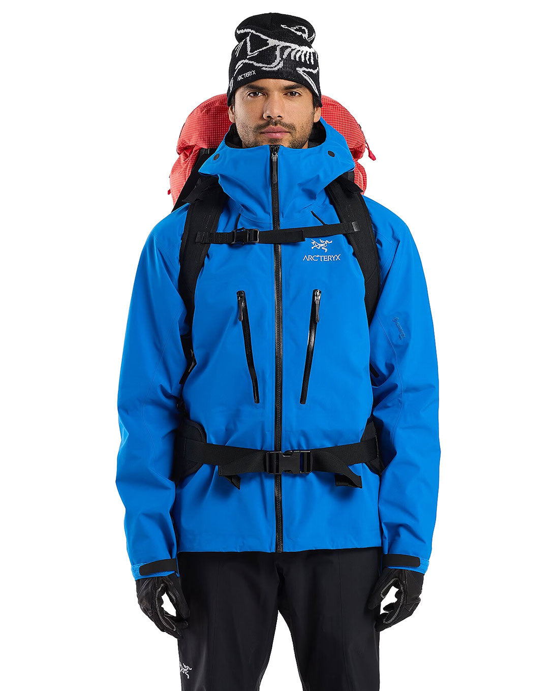 Ein Mann in einer blauen ARC'TERYX PRO Jacke, schwarzen Handschuhen, schwarzer Hose und einer Wintermütze steht mit einem Arc'teryx Rescue Pack 50 auf den Schultern mit dem Gesicht nach vorne.
