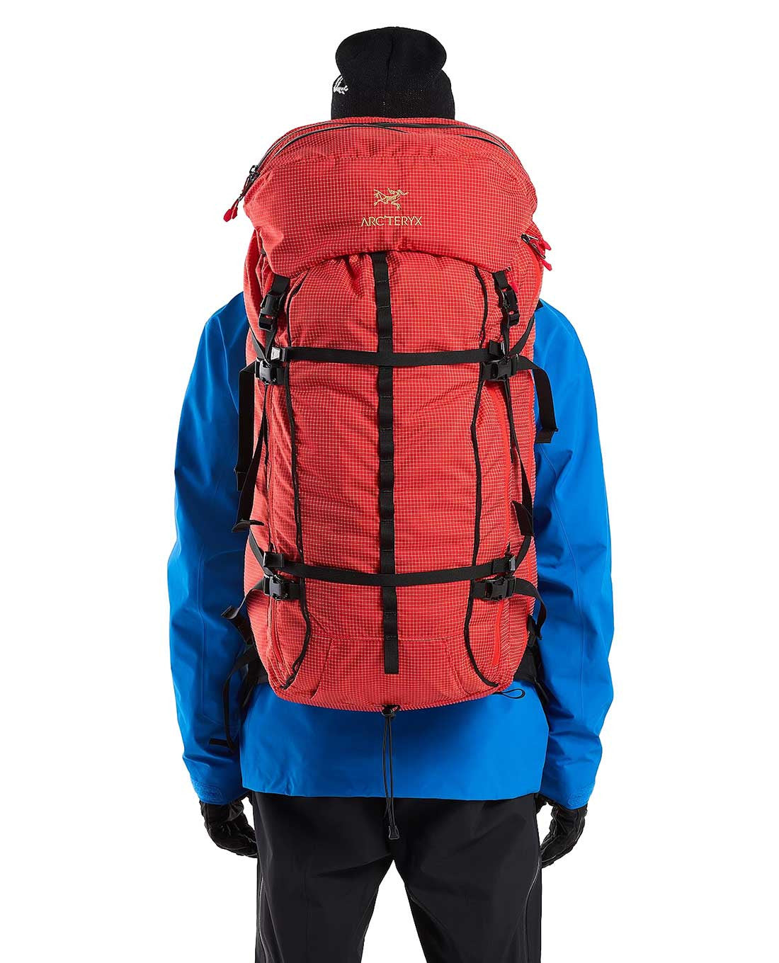 Eine Person in blauer Jacke, schwarzer Hose, Handschuhen und schwarzer Mütze ist von hinten zu sehen, die ein ARC'TERYX PRO Arc'teryx Rescue Pack 50 sicher auf den Rücken geschnallt hat.