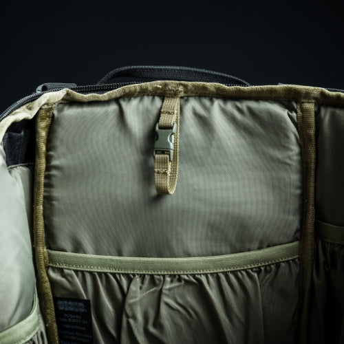 Nahaufnahme des Innenraums des EBERLESTOCK Bandit Packs mit beigem und olivgrünem Stoff, einem Schnallenriemen in der oberen Mitte, einem MOLLE-Element und mehreren elastischen Taschen auf der Rückseite.