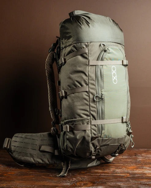 Der EBERLESTOCK Brooks 3500 in Military Green, ein geräumiger Wanderrucksack mit zahlreichen Gurten, Taschen und Schnallen, steht aufrecht auf einer Holzfläche vor braunem Hintergrund - ideal als ultraleichtes Rucksacksystem.