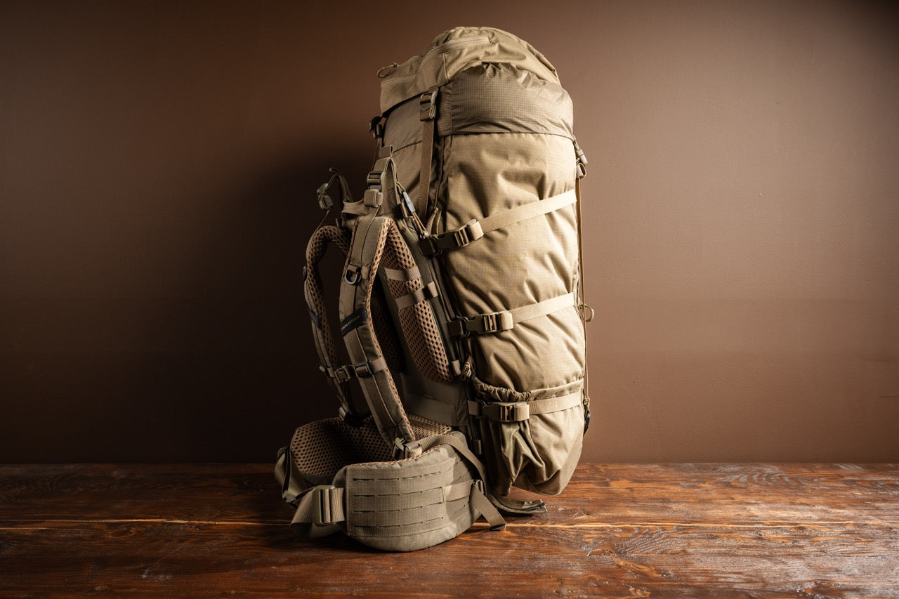 Der EBERLESTOCK Brooks 7000 in Military Green steht aufrecht auf einer rustikalen Holzoberfläche und ist bereit für Trekkingabenteuer vor einem schlichten braunen Hintergrund.