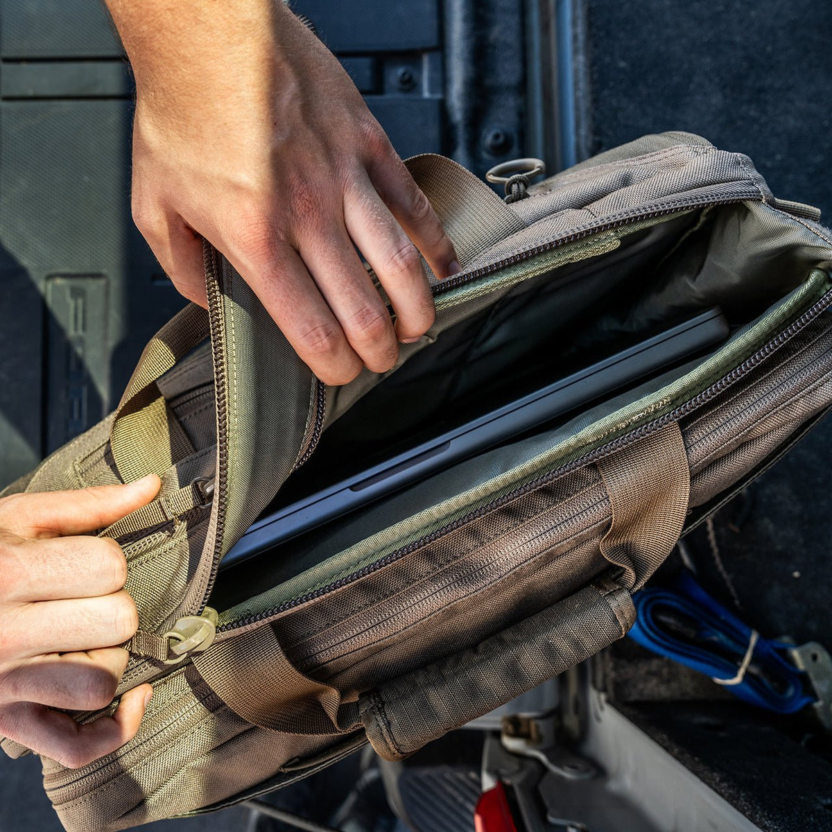 Der EBERLESTOCK Executive Brief aus strapazierfähigem 500D Cordura lässt sich mit der Hand öffnen und gibt den Blick auf einen silbernen Laptop frei. Der Slip ruht auf einer dunklen Oberfläche, während das Sonnenlicht die Szene beleuchtet.