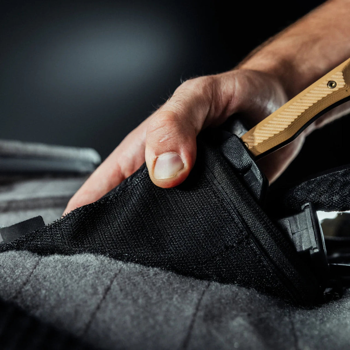Eine Nahaufnahme zeigt eine Hand, die den Holzgriff eines verdeckten Messers ergreift, das teilweise in einem schwarzen Ripstop-Nylon-Holster steckt, das an einer EBERLESTOCK Fade Admin Pouch Large befestigt ist.