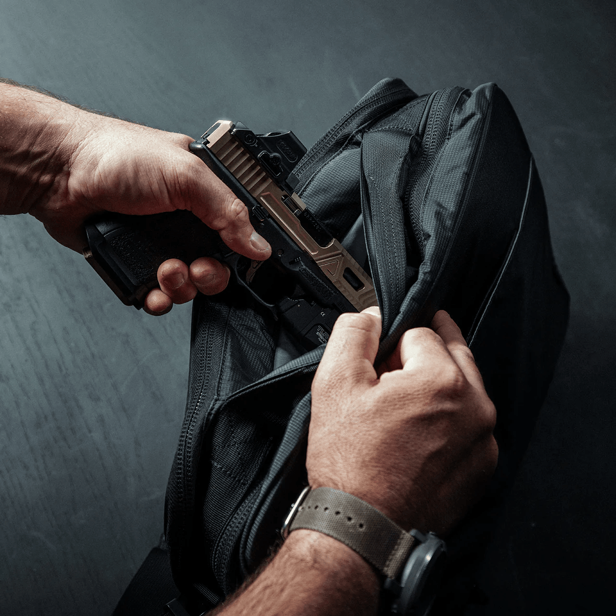 Eine Person zieht eine hellbraune und schwarze Pistole aus einem verdeckten Fach im EBERLESTOCK Fade Brief, eine Hand an der Waffe, die andere öffnet den Reißverschluss - perfekt für verdeckte Polizeiarbeit.