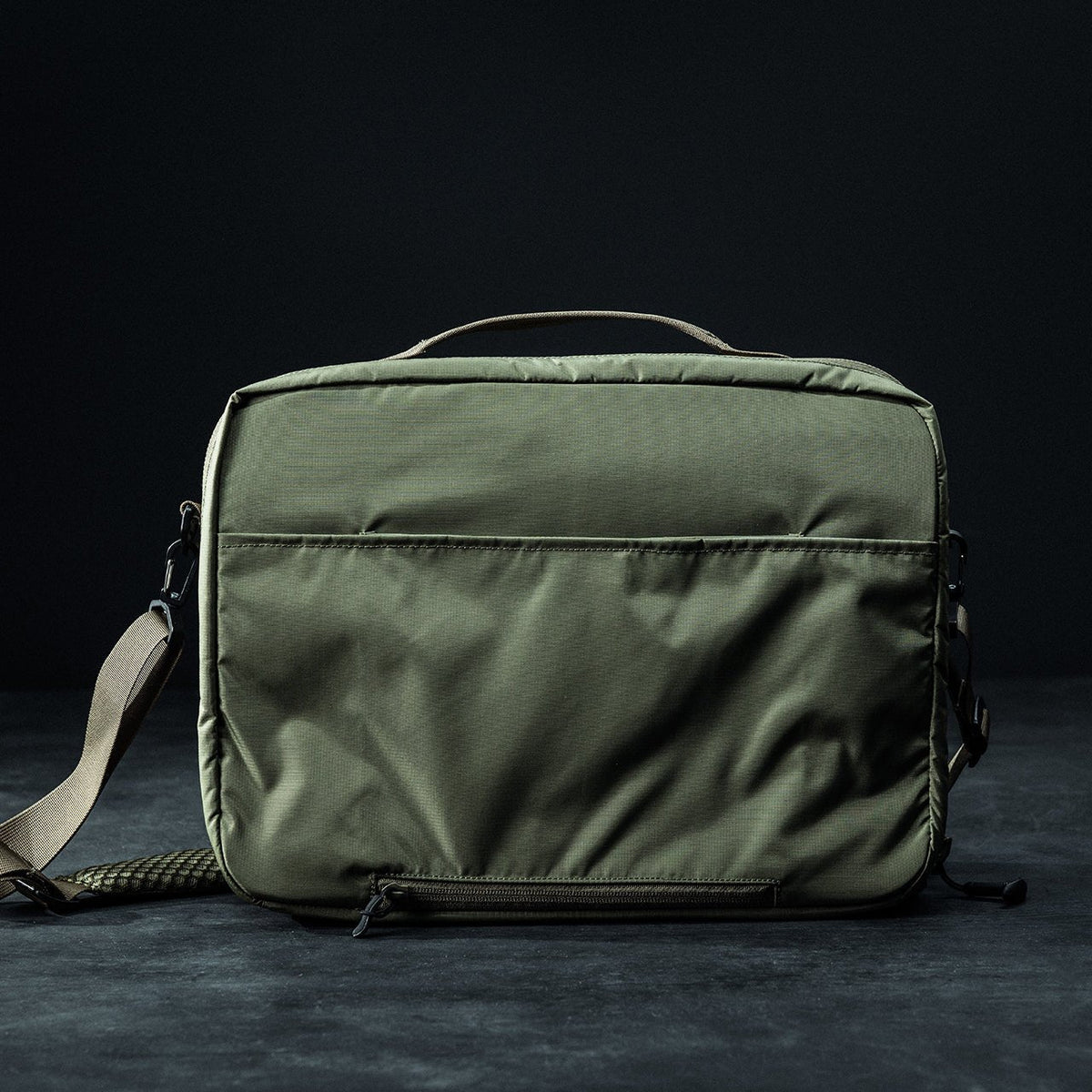 Die EBERLESTOCK Fade Brief ist eine grüne, rechteckige Umhängetasche mit einer Reißverschlusstasche auf der Vorderseite, einem Tragegriff und einem verstellbaren Schultergurt - ideal als Laptoptasche - vor einem dunklen Hintergrund.