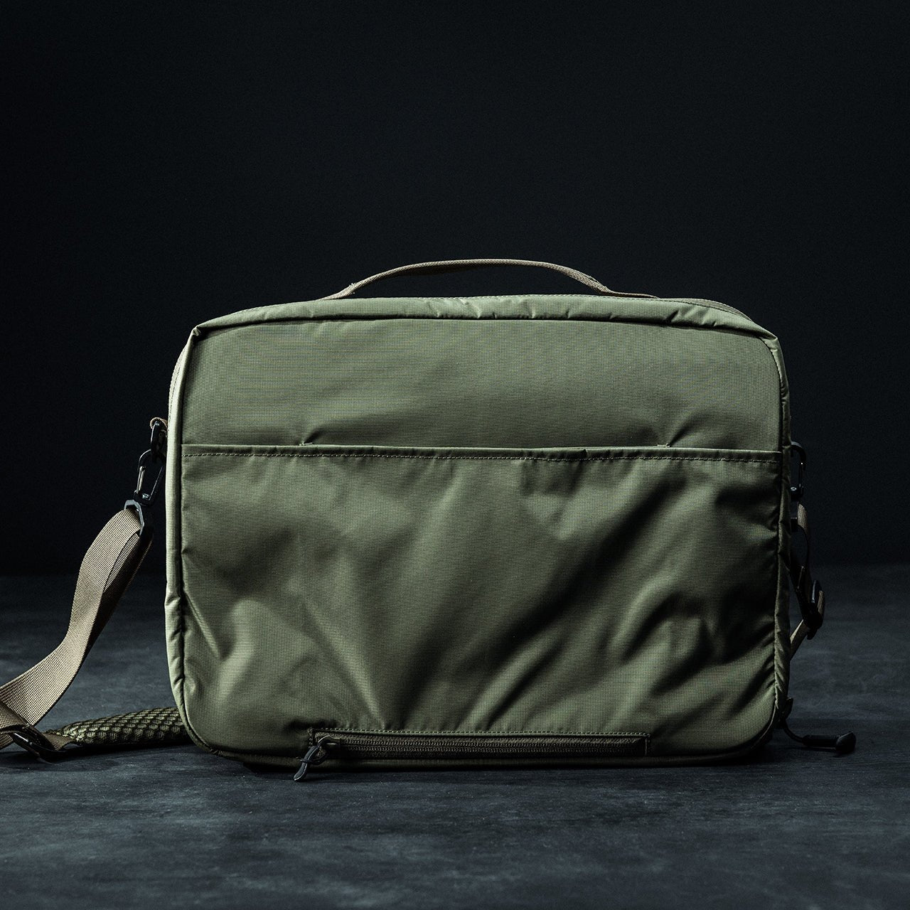Die EBERLESTOCK Eberlestock Fade Brief in Olivgrün ist eine stilvolle Laptop- und Aktentasche mit Tragegriff, verstellbarem Schultergurt und Reißverschlusstasche auf der Vorderseite - ideal für die zivile Polizeiarbeit vor dunklem Hintergrund.