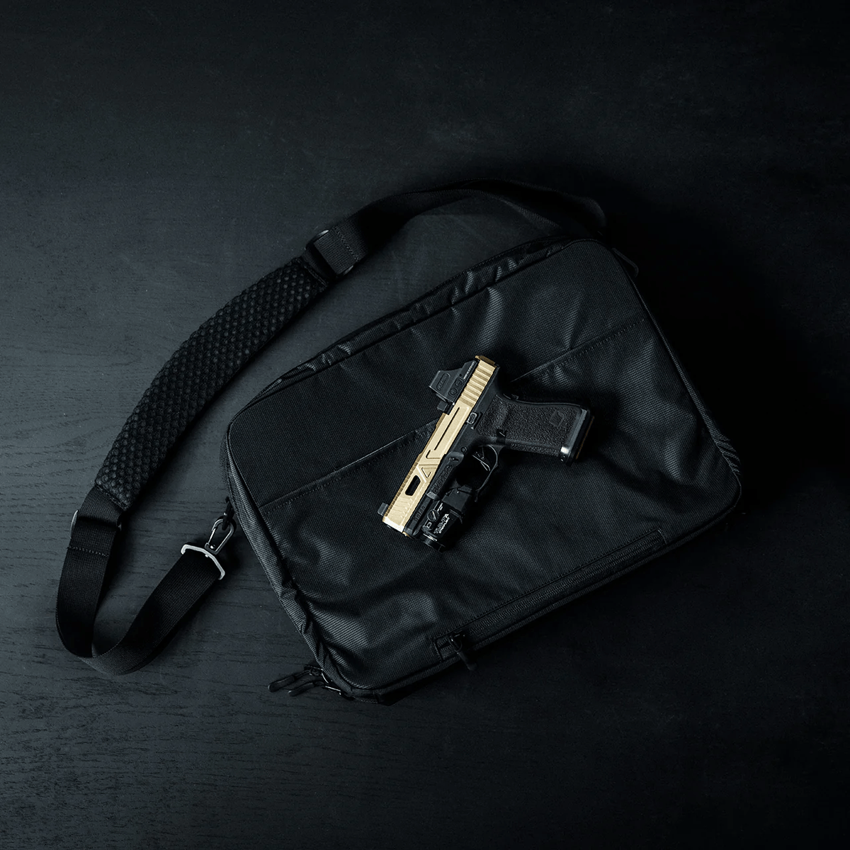 Ein schwarzer EBERLESTOCK Fade Brief ruht auf einer dunklen Oberfläche mit einer goldenen und schwarzen Handfeuerwaffe auf der Oberseite - perfekt für diskrete zivile Polizeiarbeit.