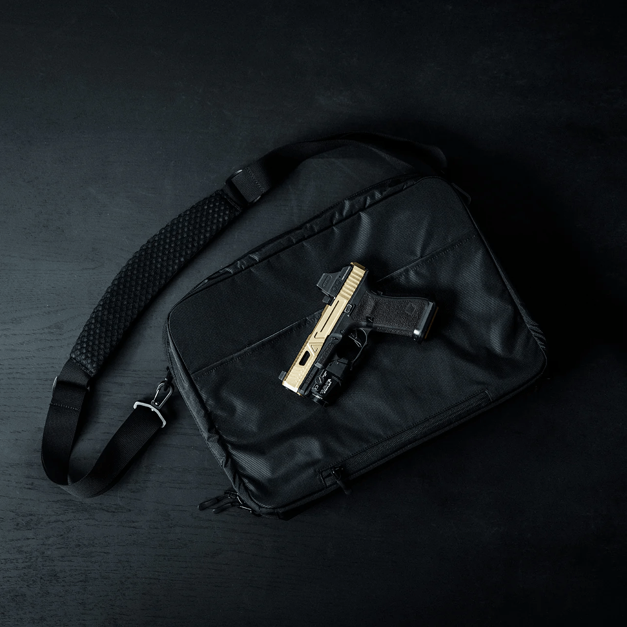 Ein schwarzer EBERLESTOCK Fade Brief ruht auf einer dunklen Oberfläche mit einer goldenen und schwarzen Handfeuerwaffe auf der Oberseite - perfekt für diskrete zivile Polizeiarbeit.
