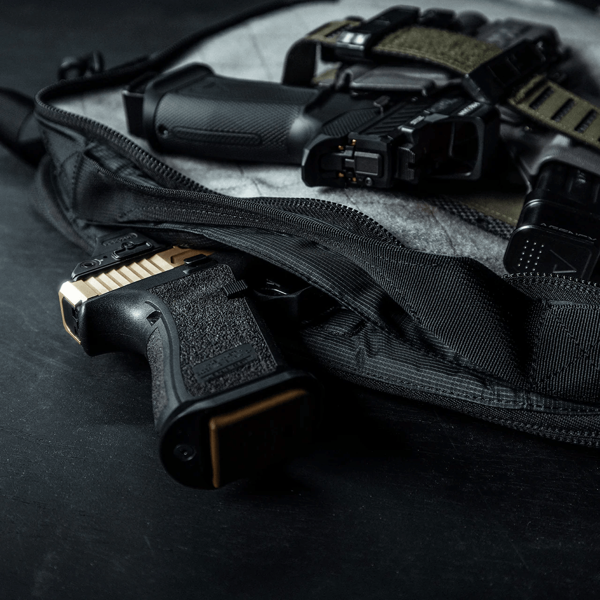 Ein schwarzer EBERLESTOCK Eberlestock Fade Brief, dessen Reißverschluss geöffnet ist, offenbart im Inneren eine halbautomatische Pistole mit braunem Schlitten, während eine zweite Pistole mit rotem Punkt und taktischer Ausrüstung, perfekt für die zivile Polizeiarbeit, obenauf liegt.