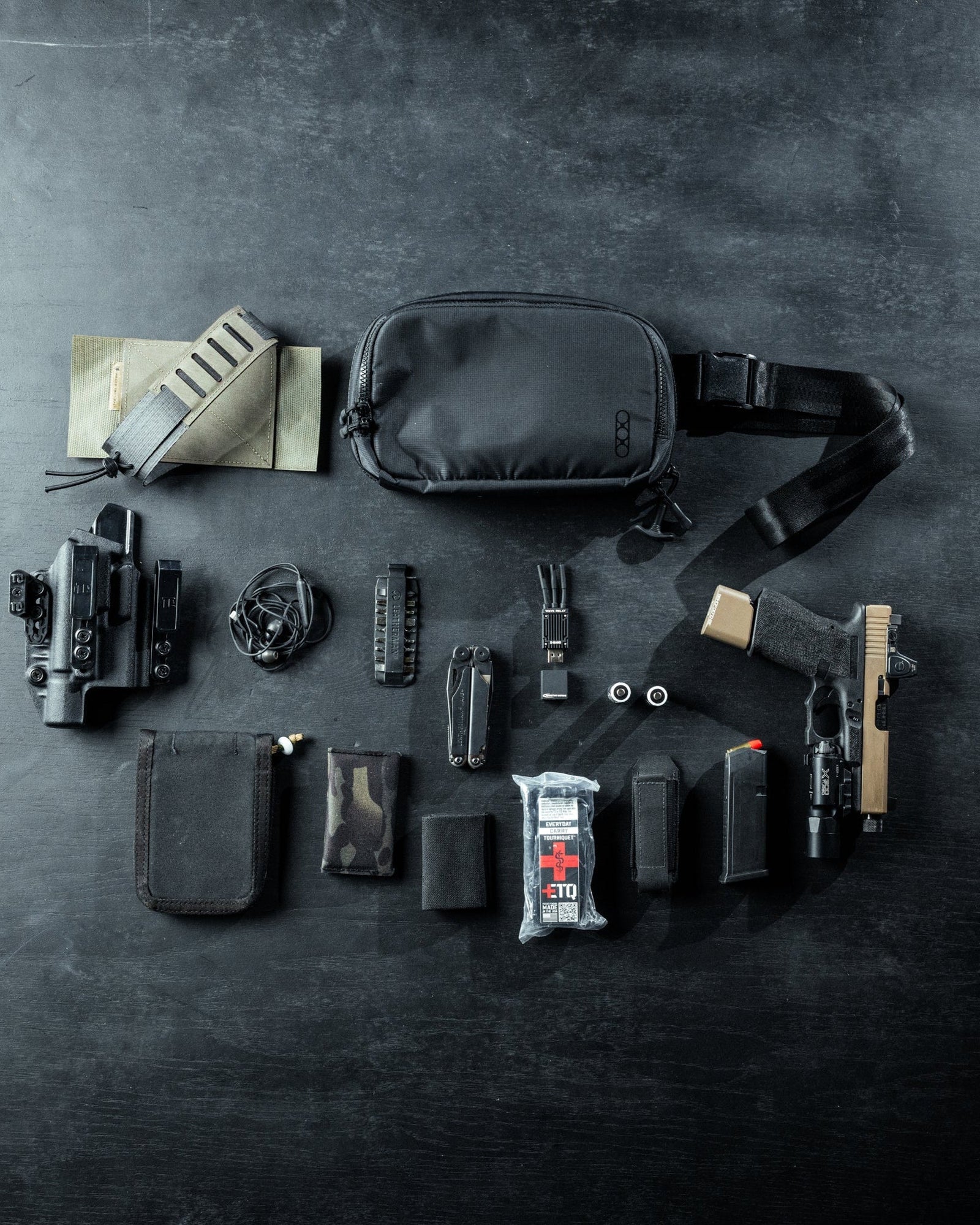Eine flache Darstellung der taktischen Ausrüstung mit der EBERLESTOCK Eberlestock Fade Flex Crossbody Bag, einer Handfeuerwaffe, einem Holster, einem Funkgerät, Munitionsmagazinen, einem Multitool, Ohrstöpseln, einem Tourniquet, einer Taschenlampe, einer Tasche und anderem Zubehör auf einer dunklen Oberfläche.