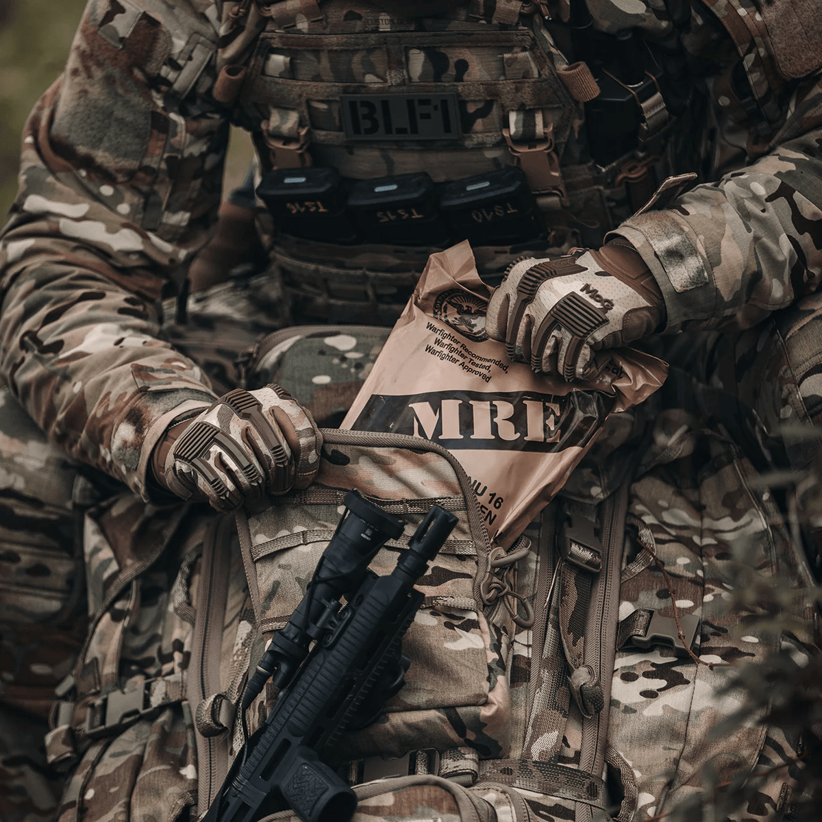 Ein Soldat in Tarnuniform und taktischer Ausrüstung holt ein MRE aus einem EBERLESTOCK G4 Operator Pack, in dessen Nähe ein Gewehr liegt.