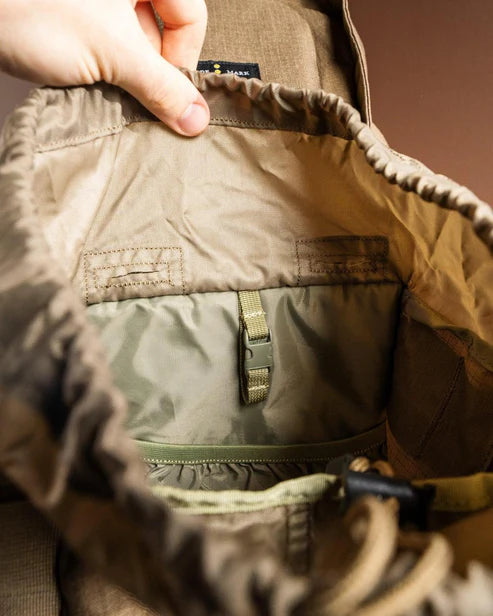 Eine Hand öffnet den EBERLESTOCK Gunrunner Pack - Mountain und zeigt sein leeres Inneres mit einer Stoffeinteilung, einer elastischen Tasche und einem zentralen Schnallenriemen - ideale Merkmale für jeden Jagdrucksack.