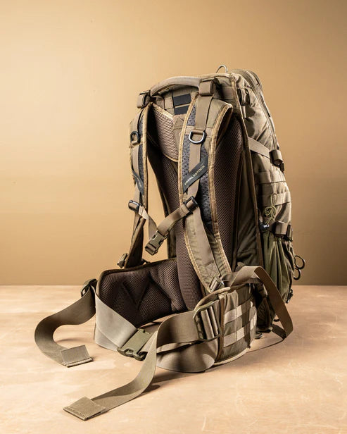 Ein schwarzer EBERLESTOCK HiSpeed II Technikrucksack mit gepolsterten Schultergurten, Netzrücken und Hüftgurt steht aufrecht auf einer beigen Fläche vor einem hellbraunen Hintergrund.