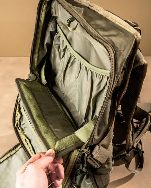 Eine Hand öffnet das vordere Fach der kojotenbraunen EBERLESTOCK HiSpeed II und zeigt organisierte Innentaschen, elastische Taschen und Reißverschlussbereiche für eine effiziente Aufbewahrung und Organisation der Ausrüstung.