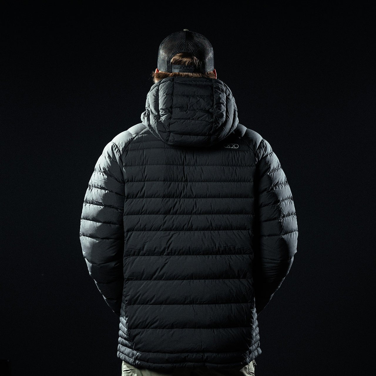 Eine Person in einem EBERLESTOCK McCall Down Hoody - Black mit Kapuze und schwarzer Mütze steht mit dem Gesicht nach unten vor einem dunklen Hintergrund.