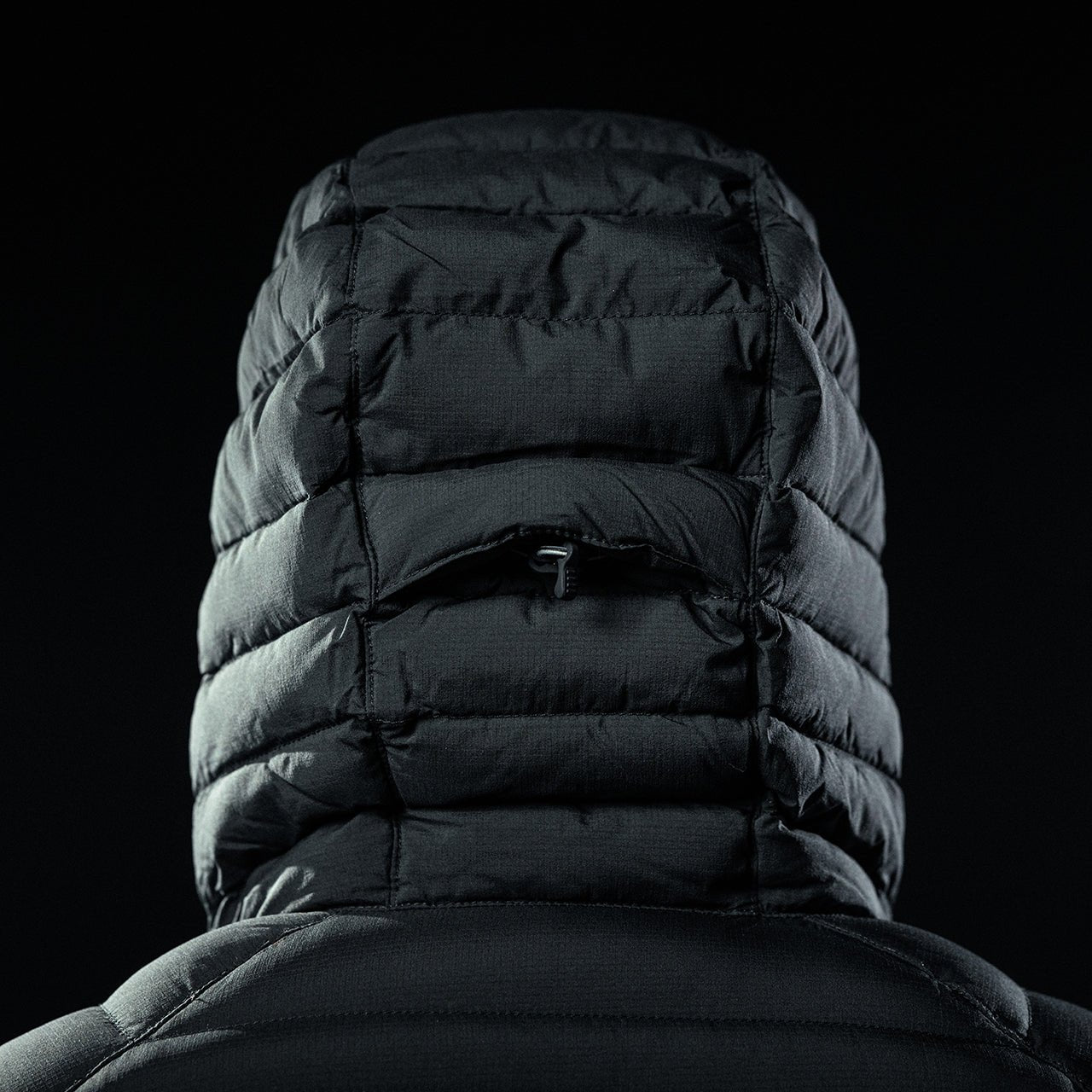 Eine Nahaufnahme von hinten zeigt eine Person, die den EBERLESTOCK McCall Down Hoody - Black mit hochgezogener Kapuze trägt, vor einem dunklen Hintergrund.