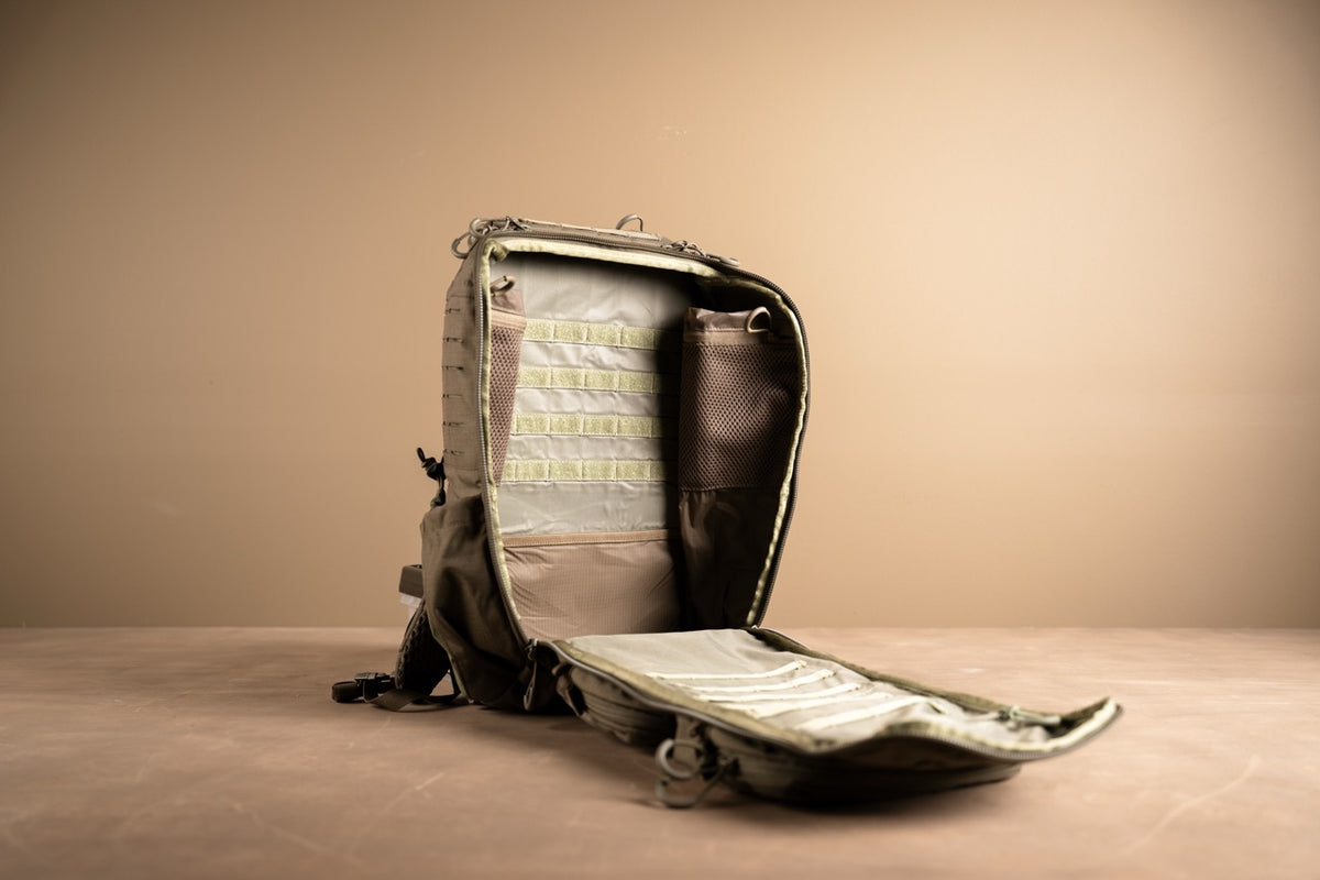 Ein schwarzer EBERLESTOCK Romad-Rucksack liegt mit geöffnetem Hauptfach auf einer braunen Fläche und zeigt organisierte Innentaschen, Mesh-Fächer, MOLLE-Gewebe und Gurte vor einem schlichten beigen Hintergrund.