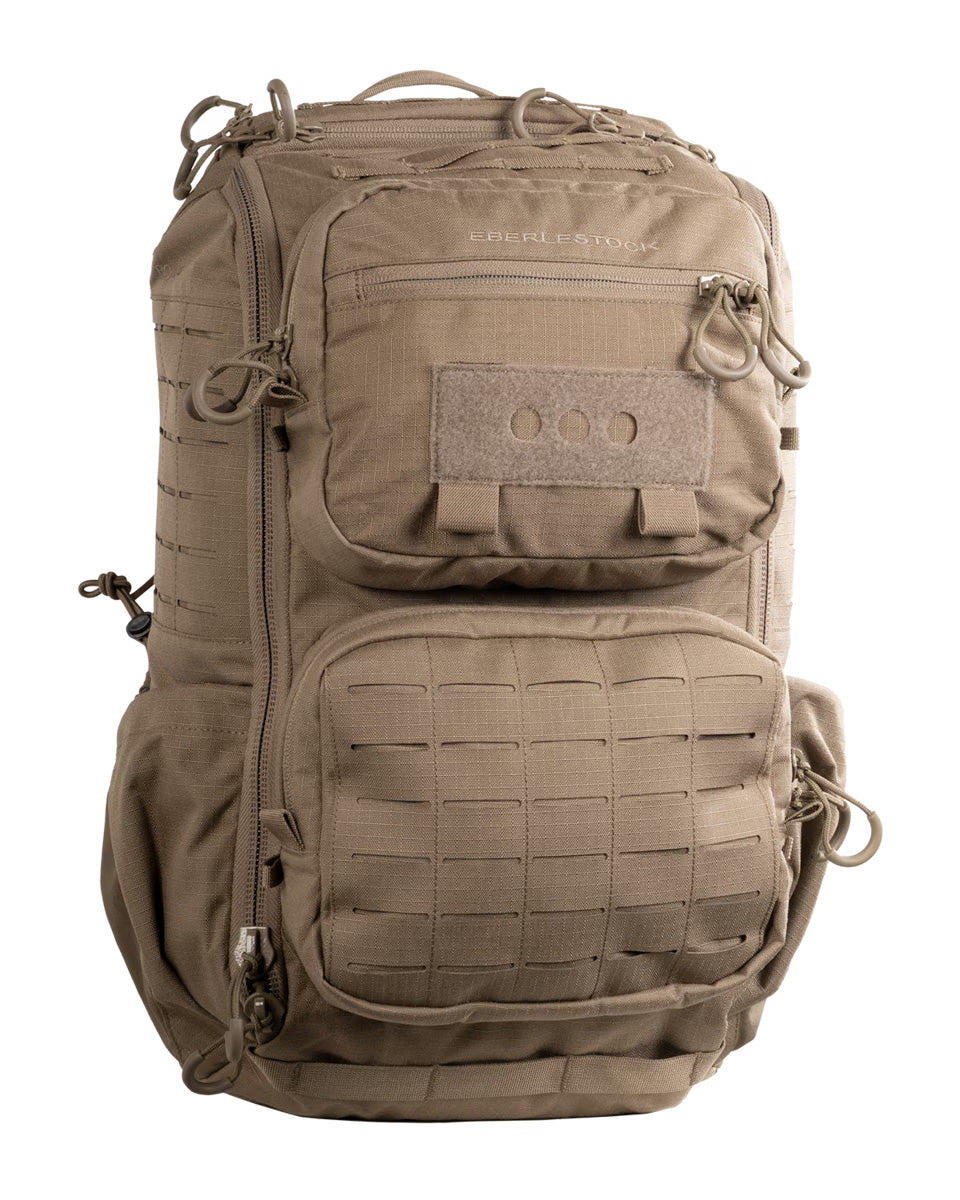 Der EBERLESTOCK Romad - Dry Earth Rucksack mit mehreren Reißverschlussfächern, Gurtband für Befestigungen, einem Tragegriff und Seitentaschen steht aufrecht vor einem weißen Hintergrund.