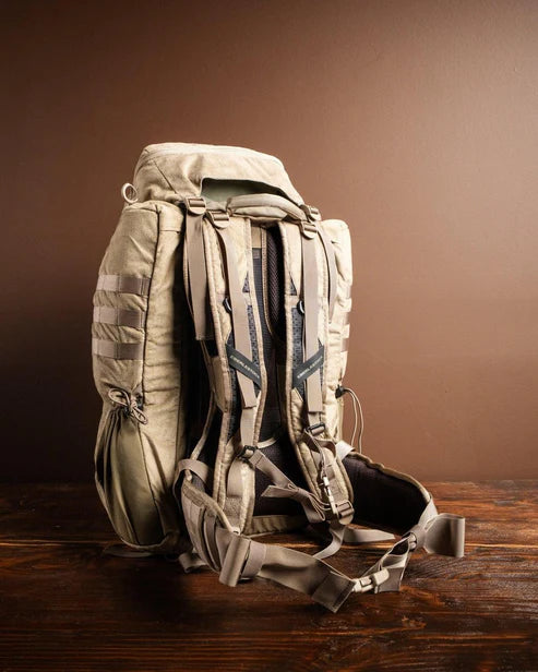 Der EBERLESTOCK X2 - Mountain, ein hellbrauner taktischer Rucksack mit 40 l Fassungsvermögen, mehreren Fächern und verstellbaren Gurten, ruht auf einer hölzernen Oberfläche vor einem braunen Hintergrund.
