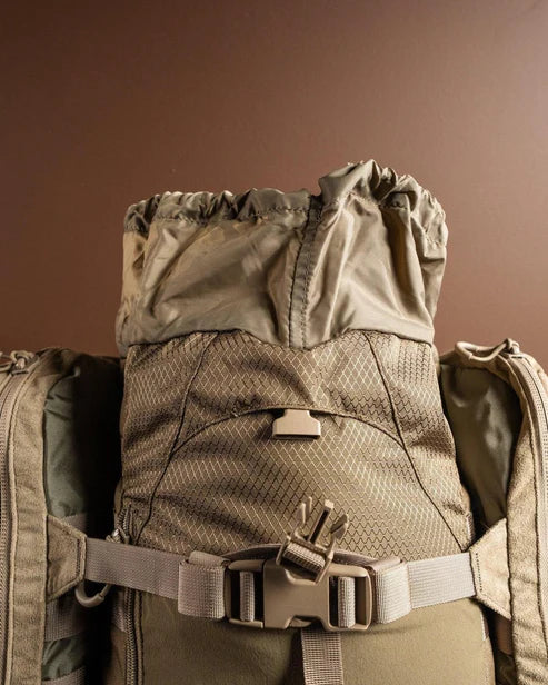 Nahaufnahme des EBERLESTOCK Eberlestock X2 - Mountain Rucksacks mit Kordelzug, Netztasche auf der Vorderseite und Schnallengurten vor einem schlichten braunen Hintergrund; er hat ein Volumen von 40 Litern.