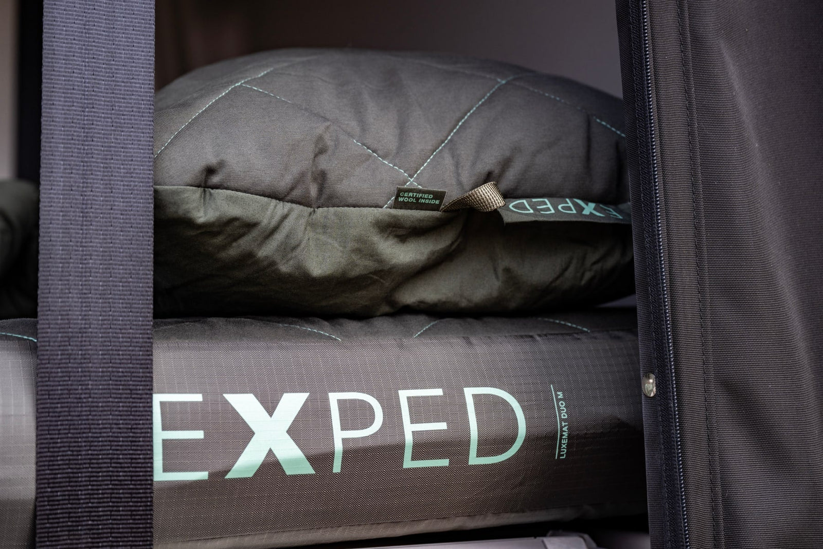 Nahaufnahme einer EXPED-Schlafmatte in Dunkelgrün mit gesteppter Decke und sichtbaren Gurten und seitlichem Reißverschluss, gepaart mit dem EXPED Kissen LuxeWool Pillow.