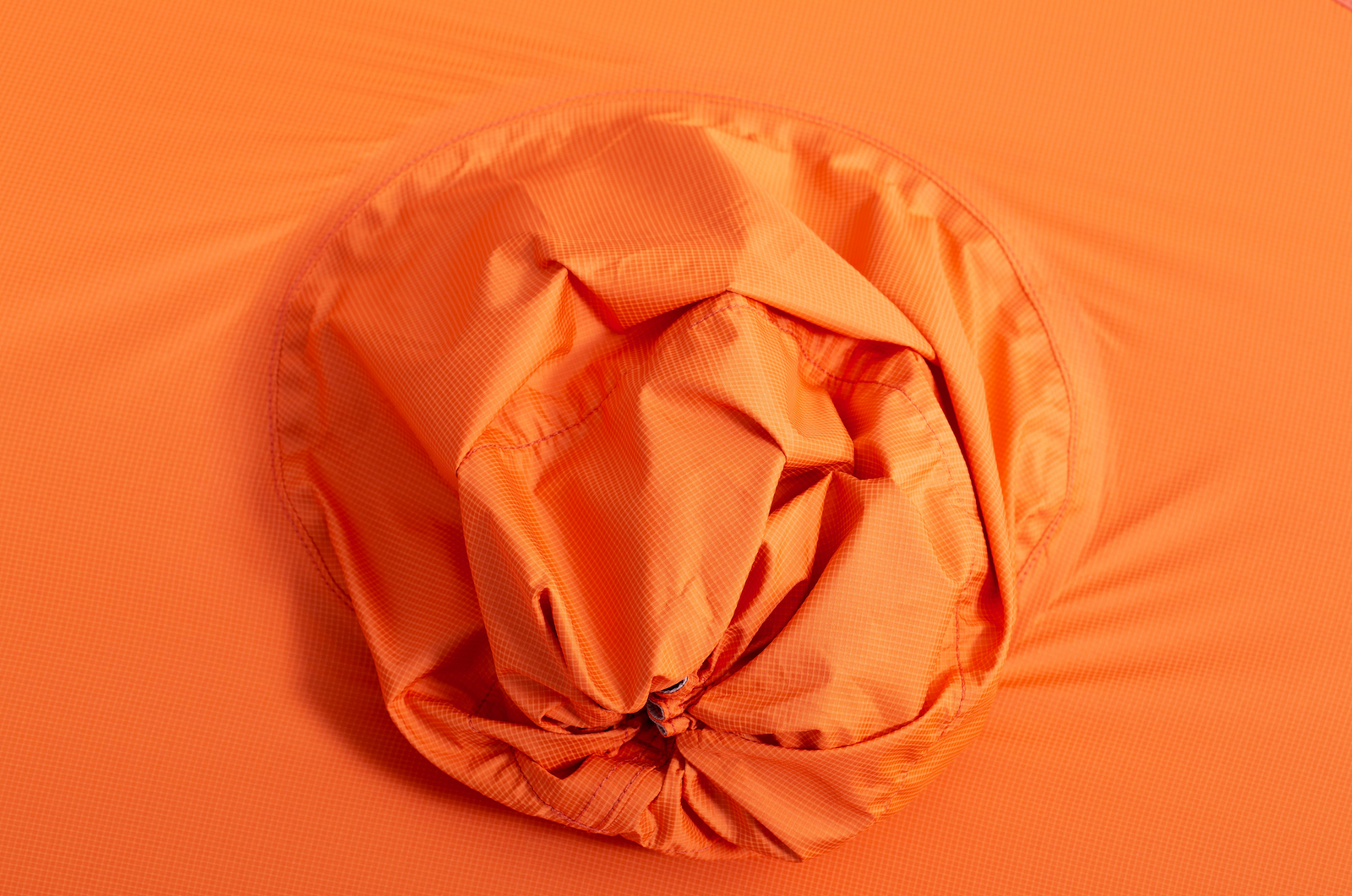 Eine Nahaufnahme des orangefarbenen Gewebes des EXPED Zelt Polaris zeigt eine kreisförmige, geraffte Mitte mit Falten und Textur. Das subtile Gittermuster trägt zum glatten, lebendigen Look dieses 4-Jahreszeiten-Expeditionszelts von EXPED bei.
