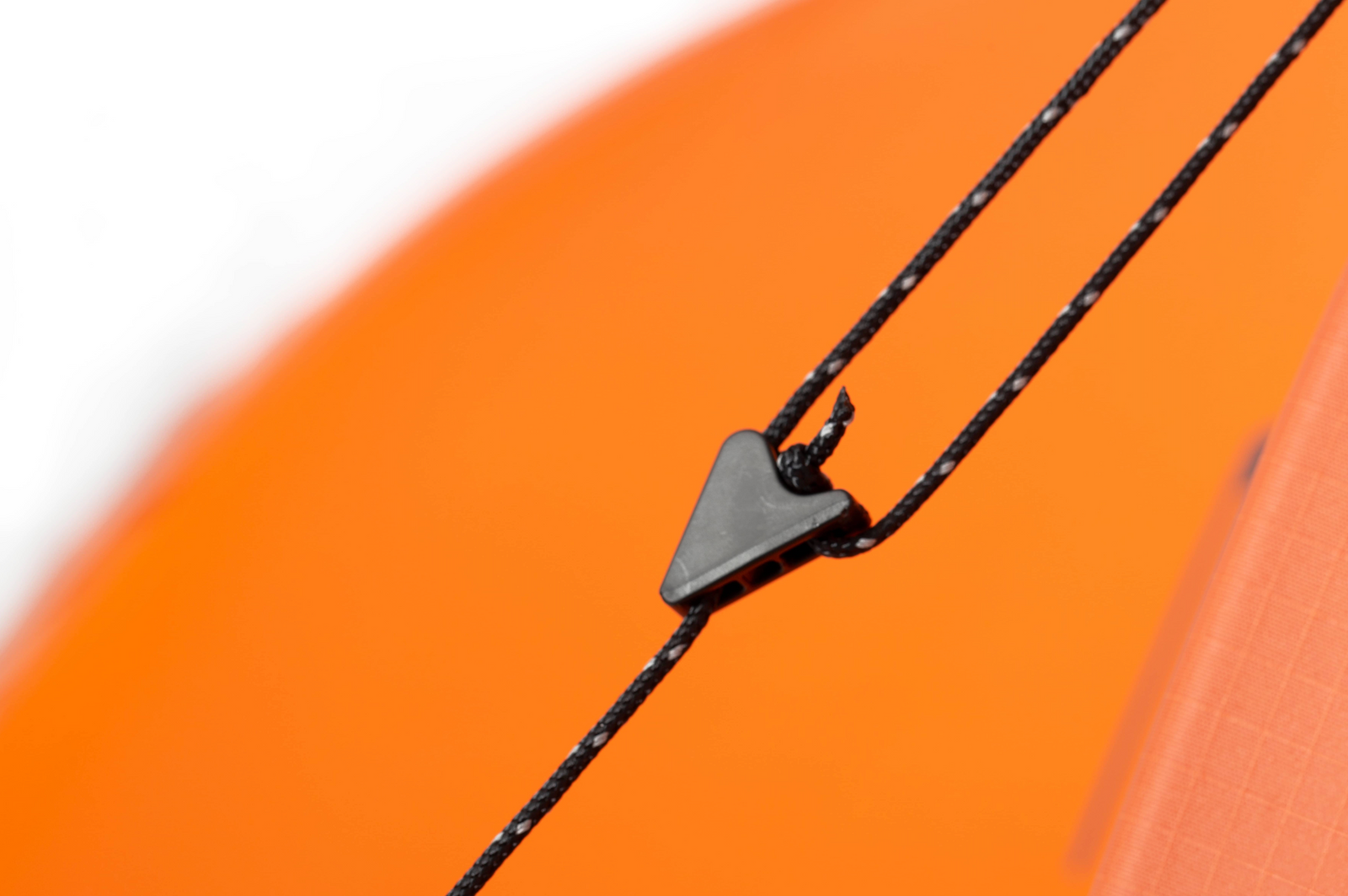 Nahaufnahme eines schwarzen Spanners, der ein schwarzes Seil am EXPED Exped Zelt Polaris, einem orangefarbenen 4-Jahreszeiten-Zelt, befestigt; der Hintergrund ist unscharf orange mit einem weißen Bereich oben links.