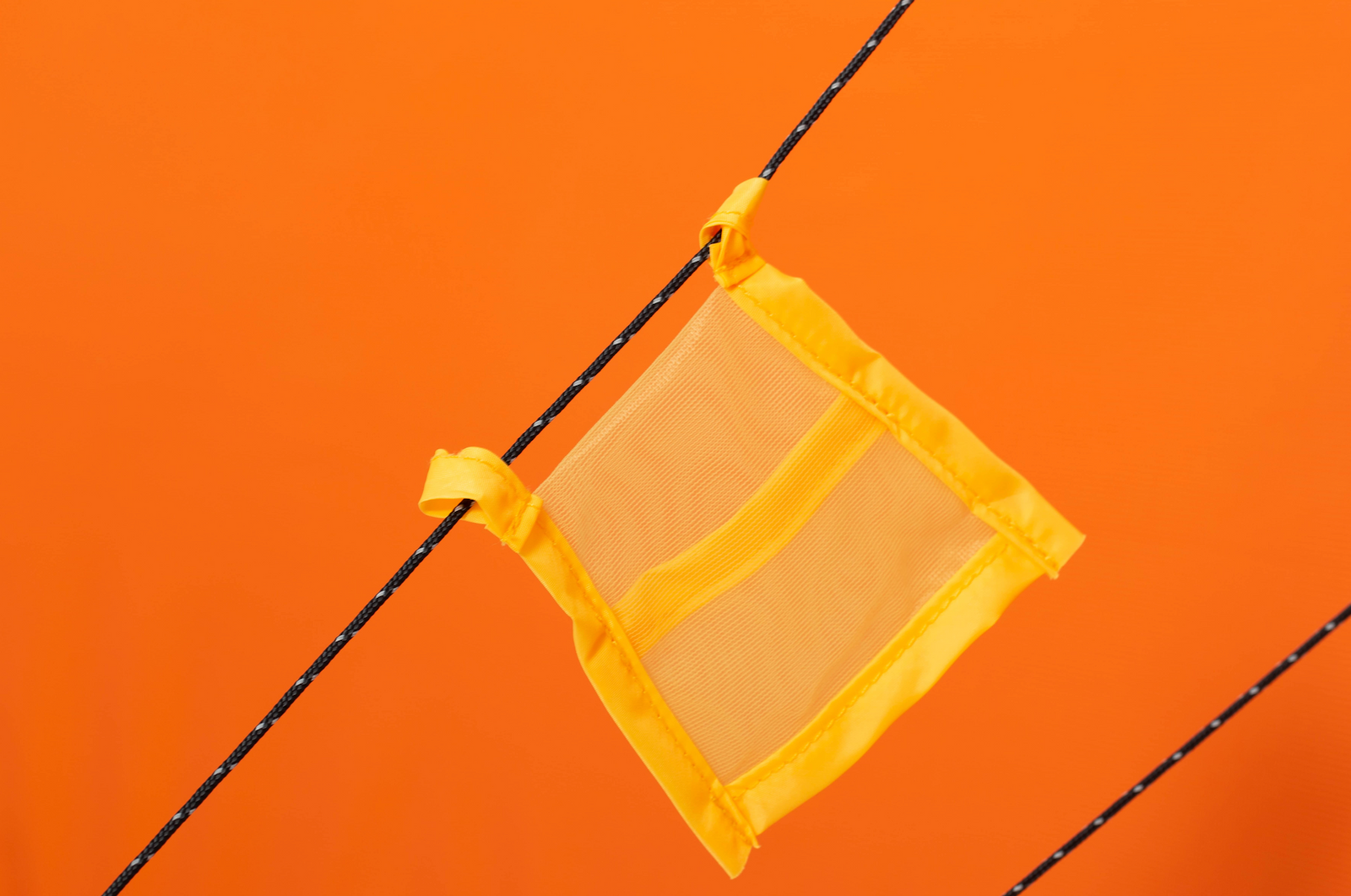 Eine kompakte gelbe Netztasche mit Stoffkanten, die an einem schwarz-weißen Seil befestigt ist, das auf einem kräftigen orangefarbenen Hintergrund abgebildet ist - ideal für die Organisation der Ausrüstung im EXPED Zelt Polaris oder in jedem 4-Jahreszeiten-Zelt während Expeditionen.