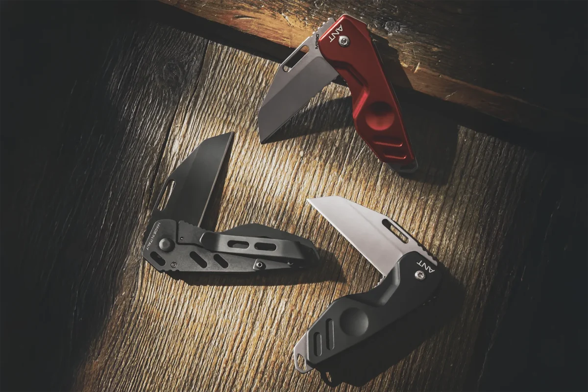 Drei Extrema Ratio Messer ANT Black Stone Washed Klappmesser von EXTREMA RATIO - zwei schwarze, ein rotes - liegen auf rustikalem Holz. Das Licht reflektiert ihre Böhler N690 Stahlklingen und betont die Schärfe und den modernen Klappmesser-Stil.