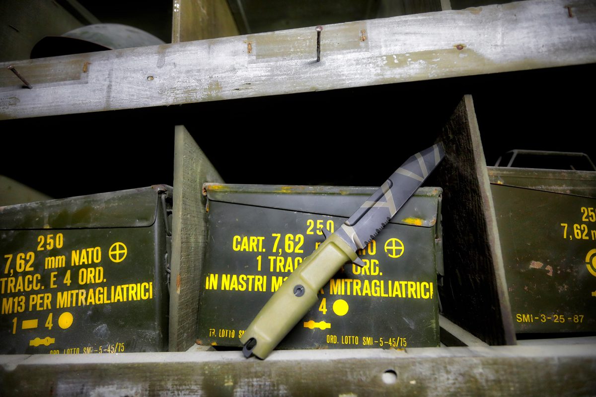 Ein EXTREMA RATIO Messer Fulcrum Desert Warfare mit grünem Griff ruht auf olivgrünen Munitionskisten mit gelber Beschriftung für 7,62 mm NATO-Munition, die in einem Metallregal gelagert sind.