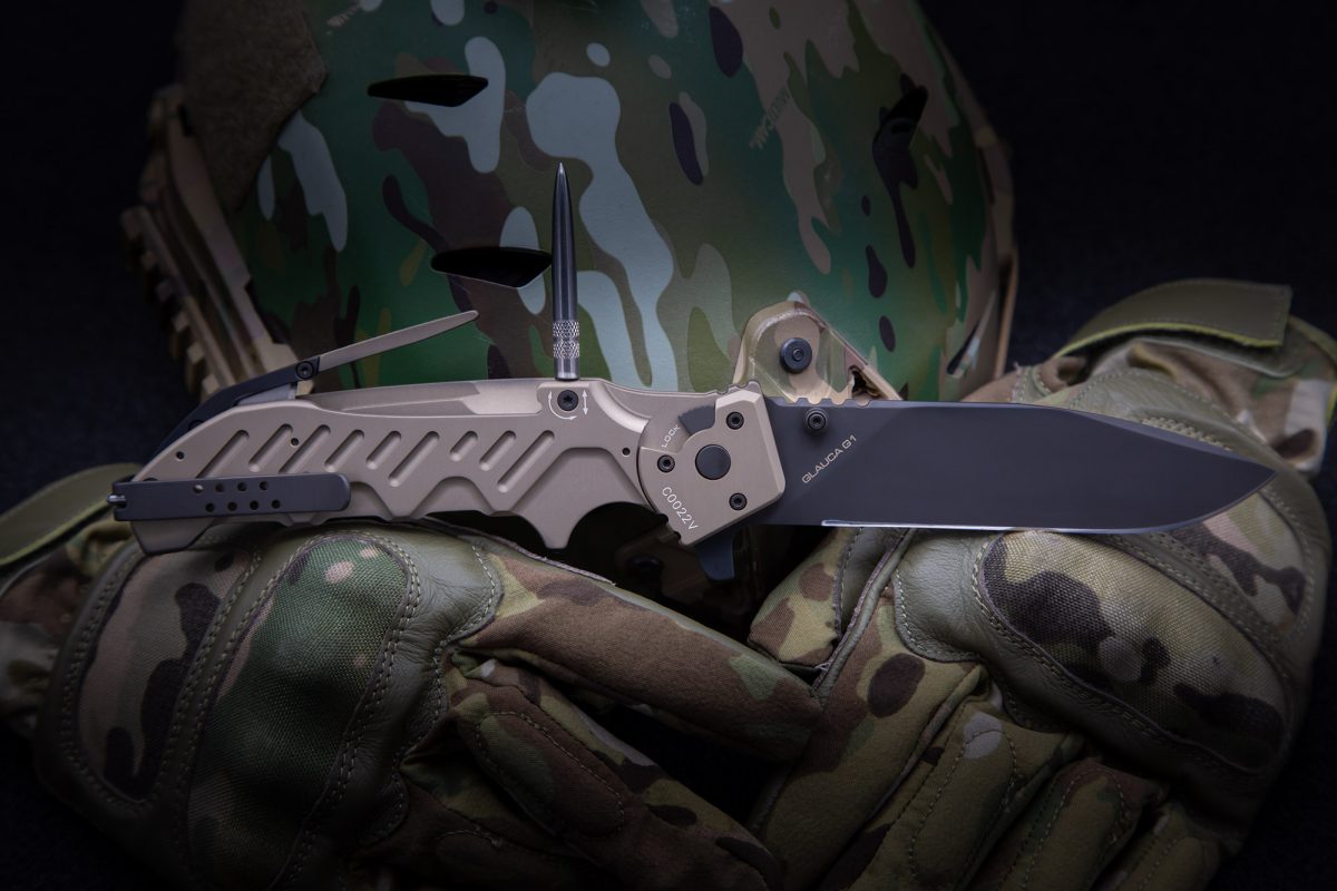 Das EXTREMA RATIO Messer Glauca G1 Klappmesser ruht auf Tarnhandschuhen, mit einem Militärhelm im Hintergrund, was seine Eignung für den taktischen oder Outdoor-Einsatz unterstreicht.