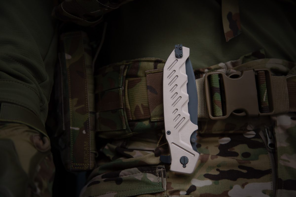 Eine Person in tarnfarbener Militärkleidung hat ein EXTREMA RATIO Extrema Ratio Messer Glauca G1 mit Metallgriff an ihrem Gürtel befestigt, der mit einer Kunststoffschnalle und Taschen ausgestattet ist. Der Fokus liegt auf dem Böhler N690 Stahlmesser und dem Torsobereich.