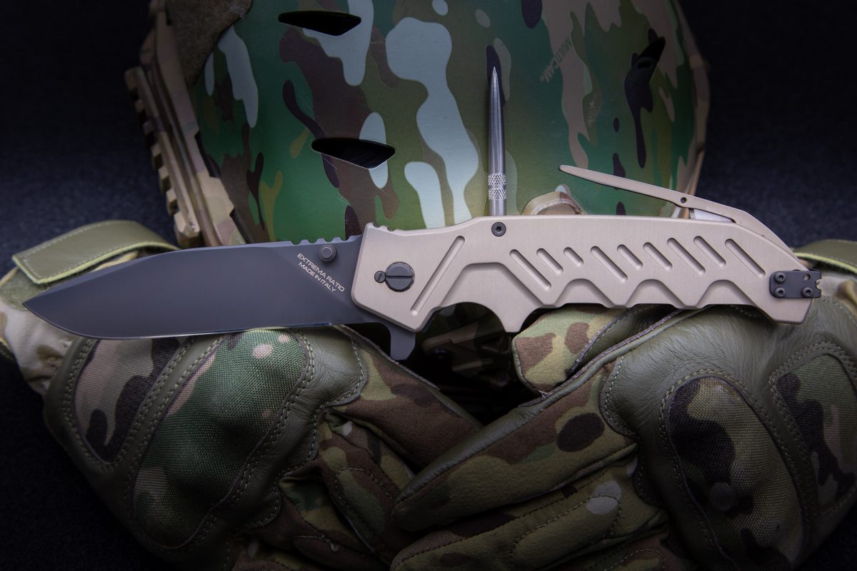 Das EXTREMA RATIO Messer Glauca G1 aus Böhler N690 Stahl liegt auf tarnfarbenen Handschuhen, im Hintergrund sind ein Camouflage-Helm und ein metallisches Werkzeug zu sehen.