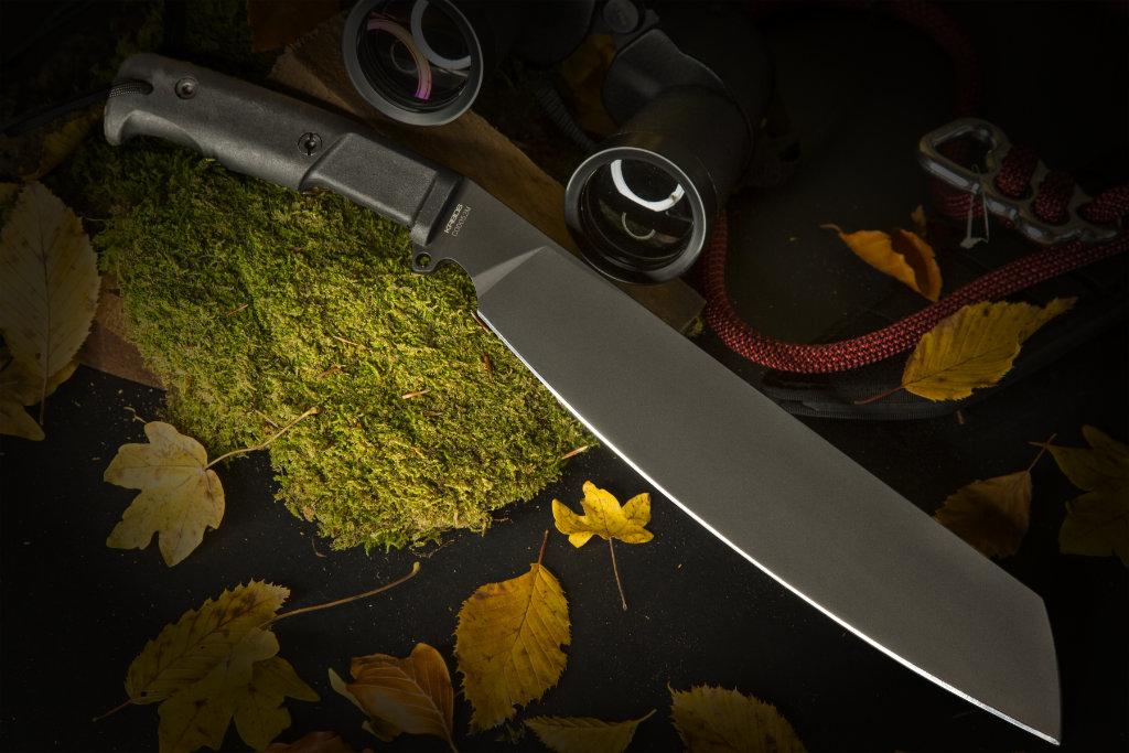 Das Extrema Ratio Messer Kreios von EXTREMA RATIO mit schwarzem Griff ruht auf bemooster Rinde, umgeben von Herbstblättern, einem roten Seil, einem Fernglas und einem Metallkarabiner auf einer dunklen Fläche.