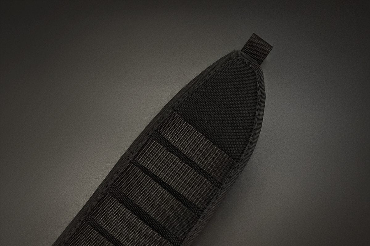 Nahaufnahme eines schwarzen Nylonbandes mit verstärkten Kanten und einer oberen Schlaufe, das das EXTREMA RATIO Messer Numen S600 Black auf einem dunklen Hintergrund mit Farbverlauf sicher hält. Horizontale Nähte sorgen für zusätzliche Festigkeit und Haltbarkeit.