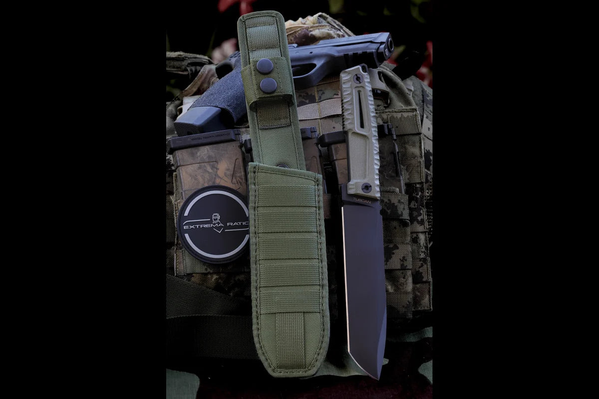 Das EXTREMA RATIO Messer Tuscan Green steht aufrecht auf Tarnkleidung neben einem schwarzen EXTREMA RATIO Kanister und einer teilweise sichtbaren Handfeuerwaffe. Gefertigt aus Böhler N690 Stahl, ist dieses Messer für anspruchsvolle Einsätze konzipiert.
