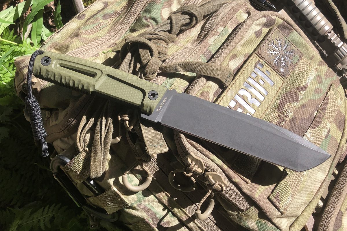 Ein EXTREMA RATIO Messer Tuscan Green mit grünem Griff ruht auf einem Tarnrucksack im Freien. Das Sonnenlicht hebt die Böhler N690 Stahlklinge und die taktische Ausrüstung um sie herum hervor.