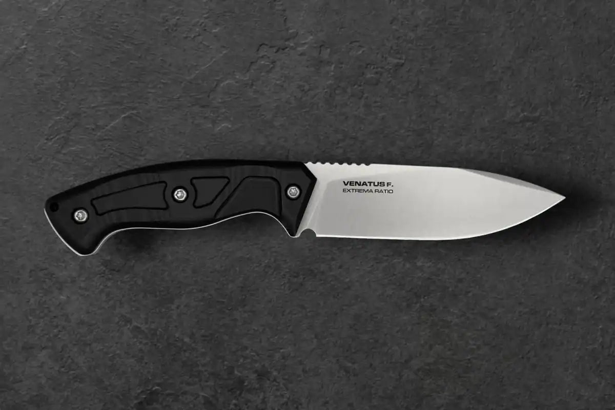 Das EXTREMA RATIO Venatus F Black Satin ist ein feststehendes Outdoormesser mit einer polierten Böhler N690 Stahlklinge und einem schwarz strukturierten Griff, der auf einer dunkelgrauen Steinoberfläche abgebildet ist.