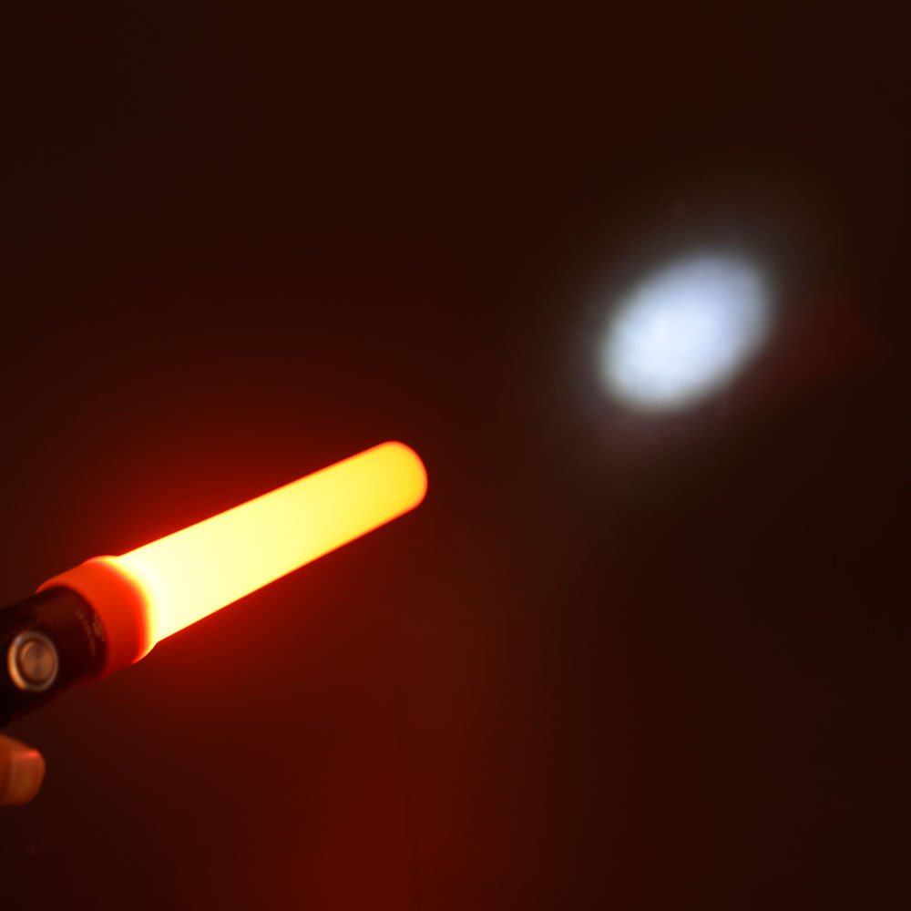 Eine Hand hält eine FITORCH-Taschenlampe mit dem Fitorch Signalkegel FT-1 in der Hand. Der orange-rote Kegel leuchtet und wirft einen hellen weißen Fleck auf einen dunklen Hintergrund.