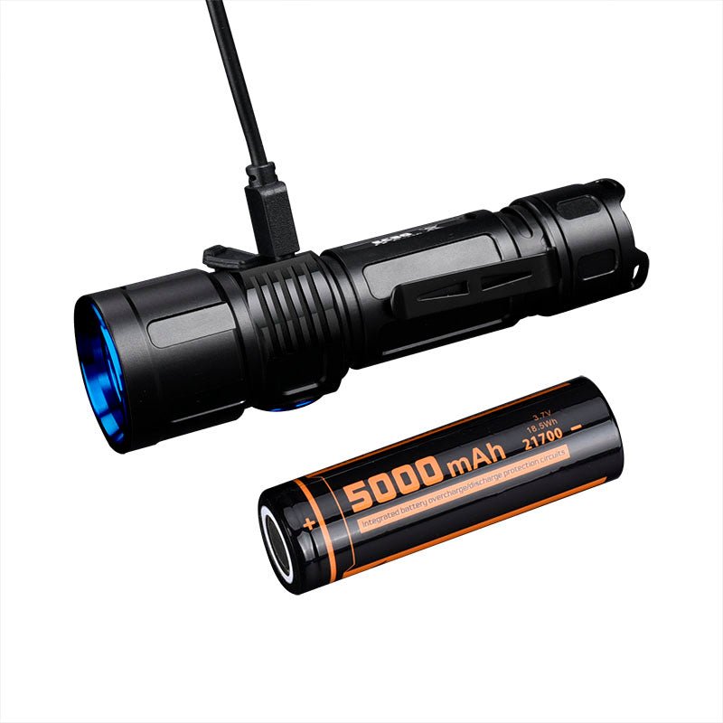 Eine FITORCH Taschenlampe EC30 in Schwarz wird per Kabel geladen, daneben liegt ein 5000mAh 21700 Akku.