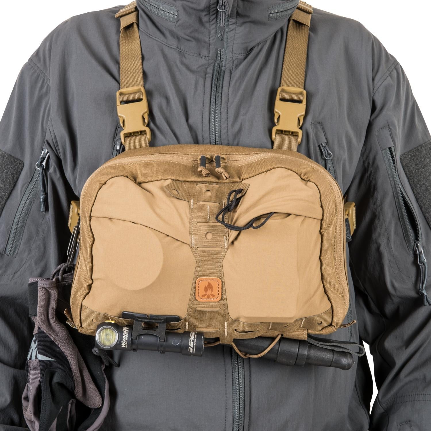 Die Person ist mit einer grauen Jacke bekleidet und trägt einen HELIKON-TEX Chest Pack Numbat® in Earth Brown/Clay B, der über mehrere Taschen, Schnallen, eine angeklippte Taschenlampe, einen Stift in der Brusttasche und eine schwarze Frontkordel verfügt.
