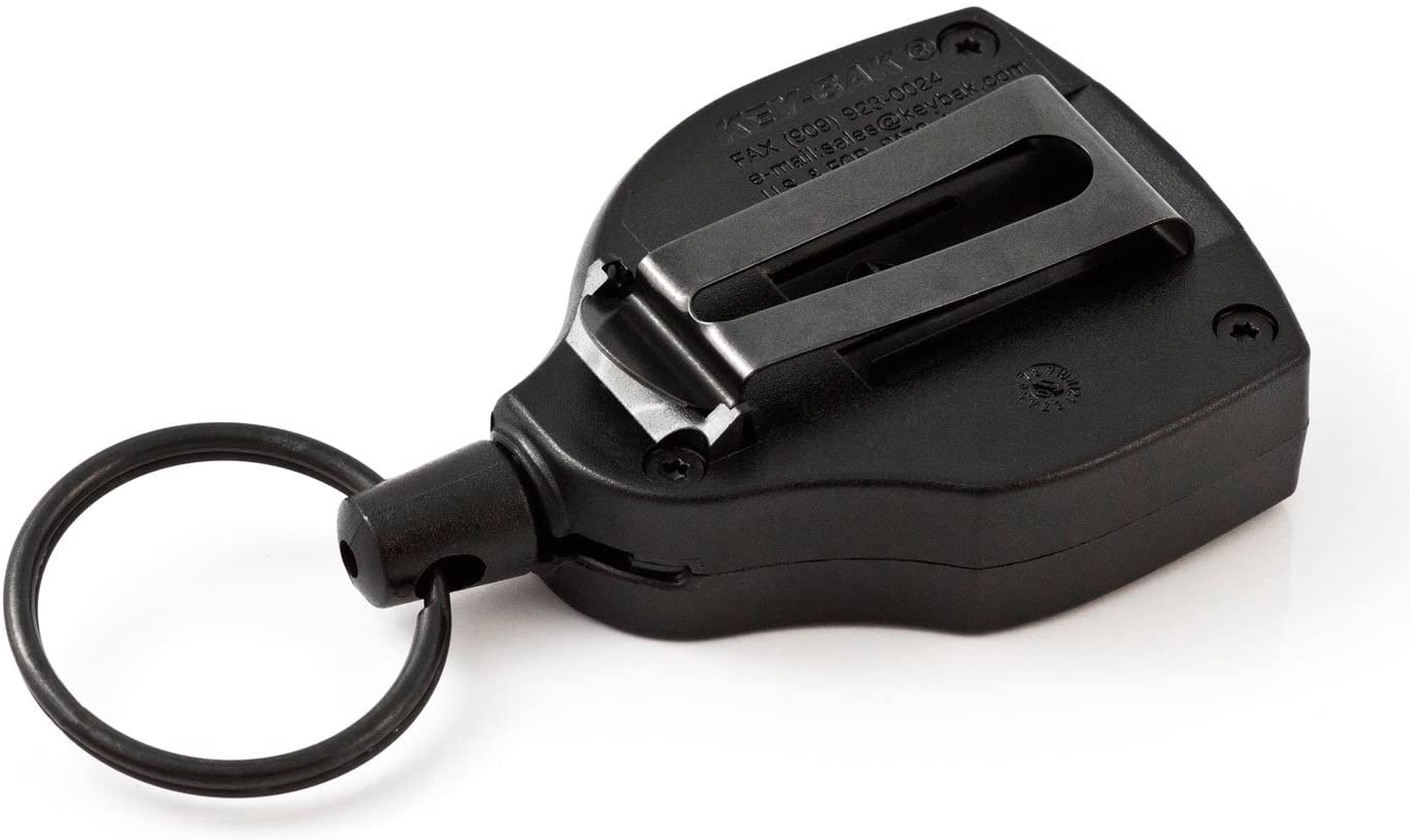Ein schwarzer KEY-BAK Key-Bak Schlüsselhalter mit einem Gurtclip aus Metall auf der Rückseite und einem runden Schlüsselring an einem Ende, der auf einer weißen Fläche ruht.